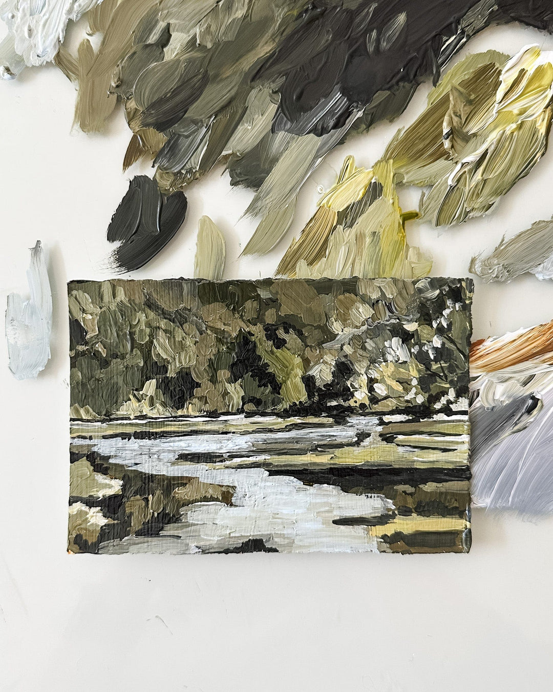 Painting of a landscape with a river, surrounded by paint swatches.