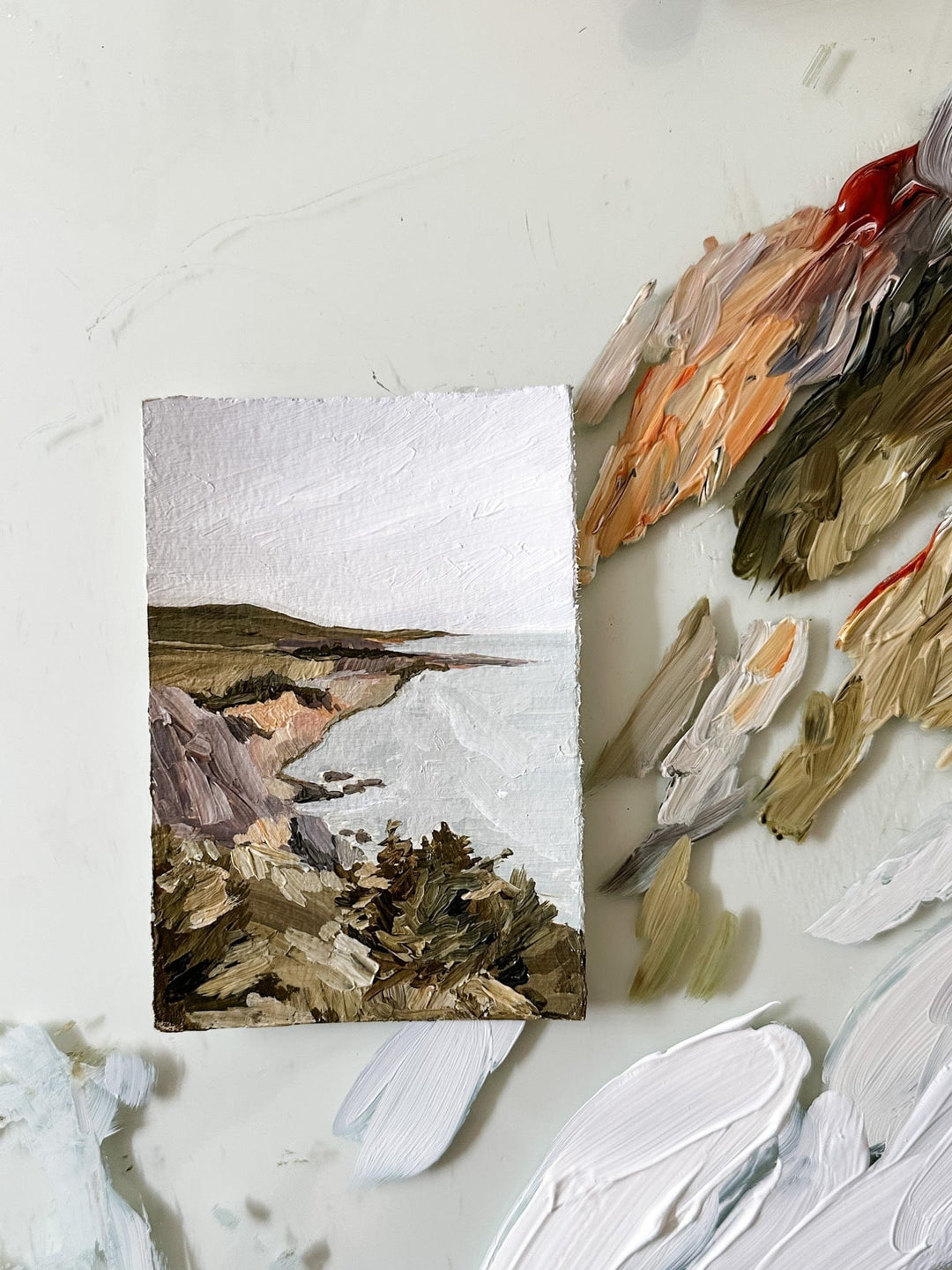 Painting of a coastal landscape with a palette of paint.