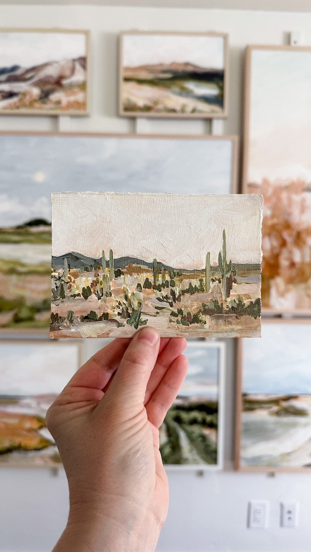 Hand holding painting of desert landscape.