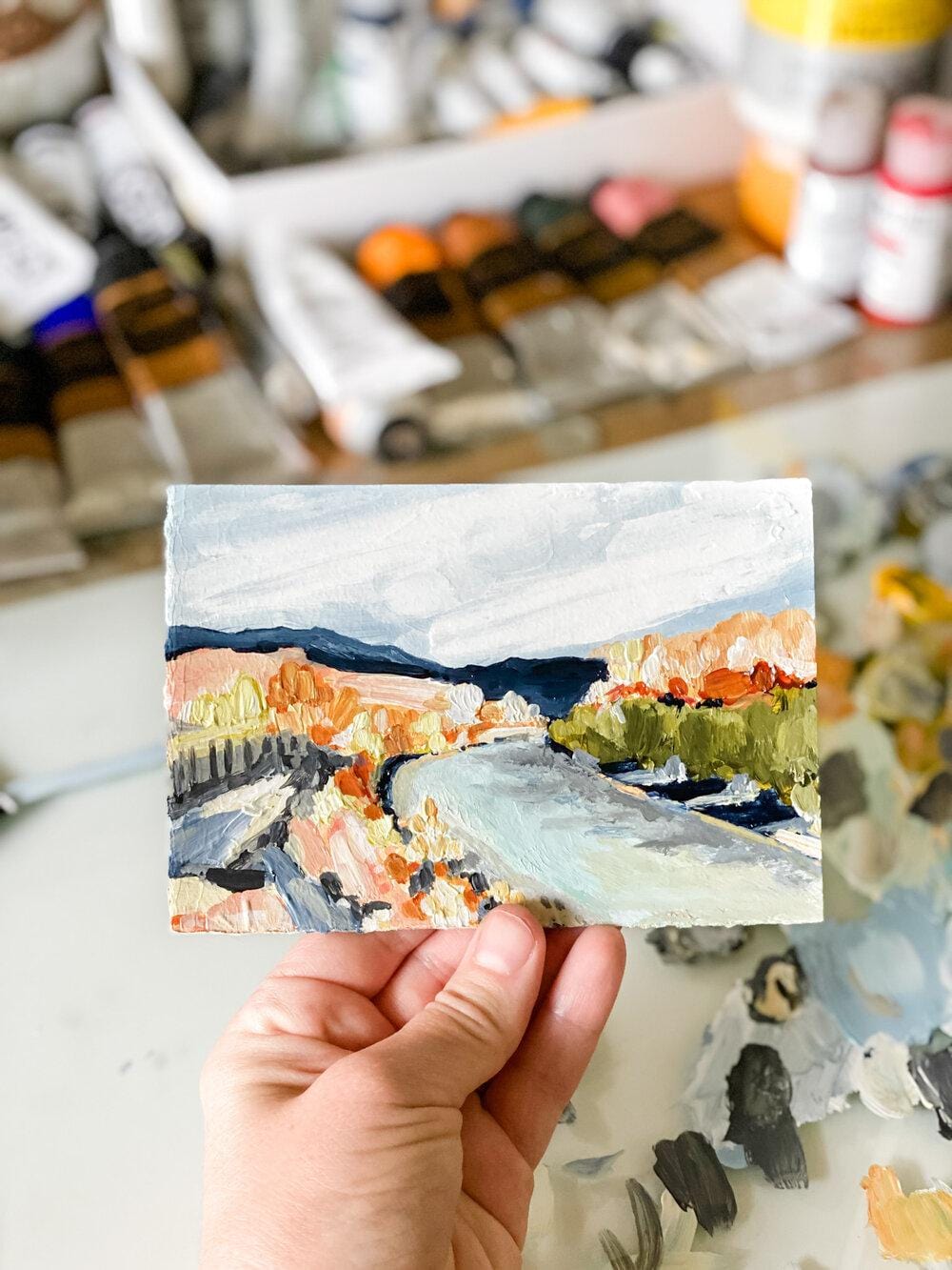 Hand holding a small landscape painting.