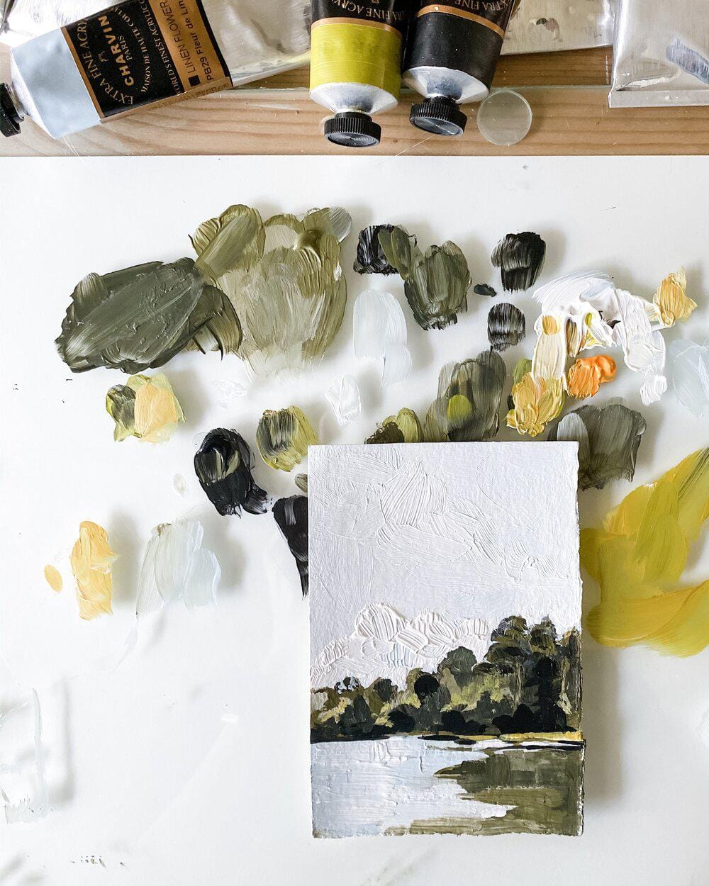 Painting palette with landscape art and paint tubes.
