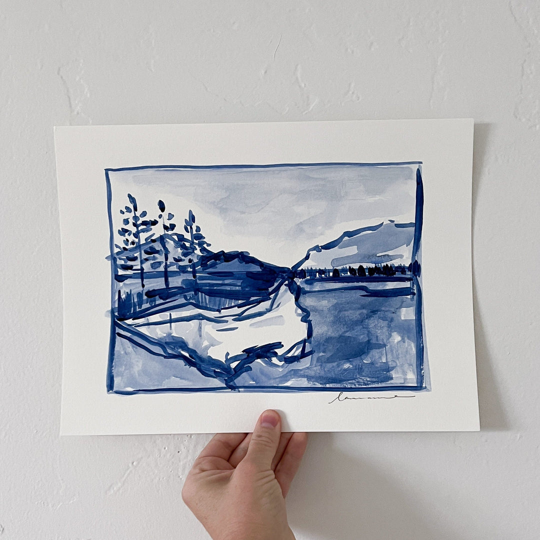 Watercolor painting of a lake and mountains, held by a hand.