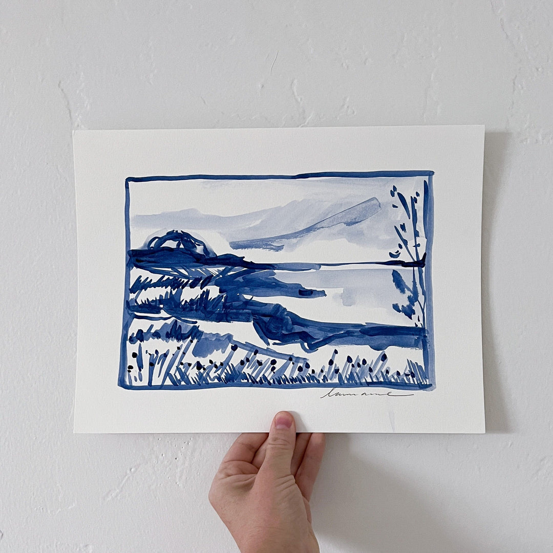 Watercolor landscape painting in blue, held by a hand.