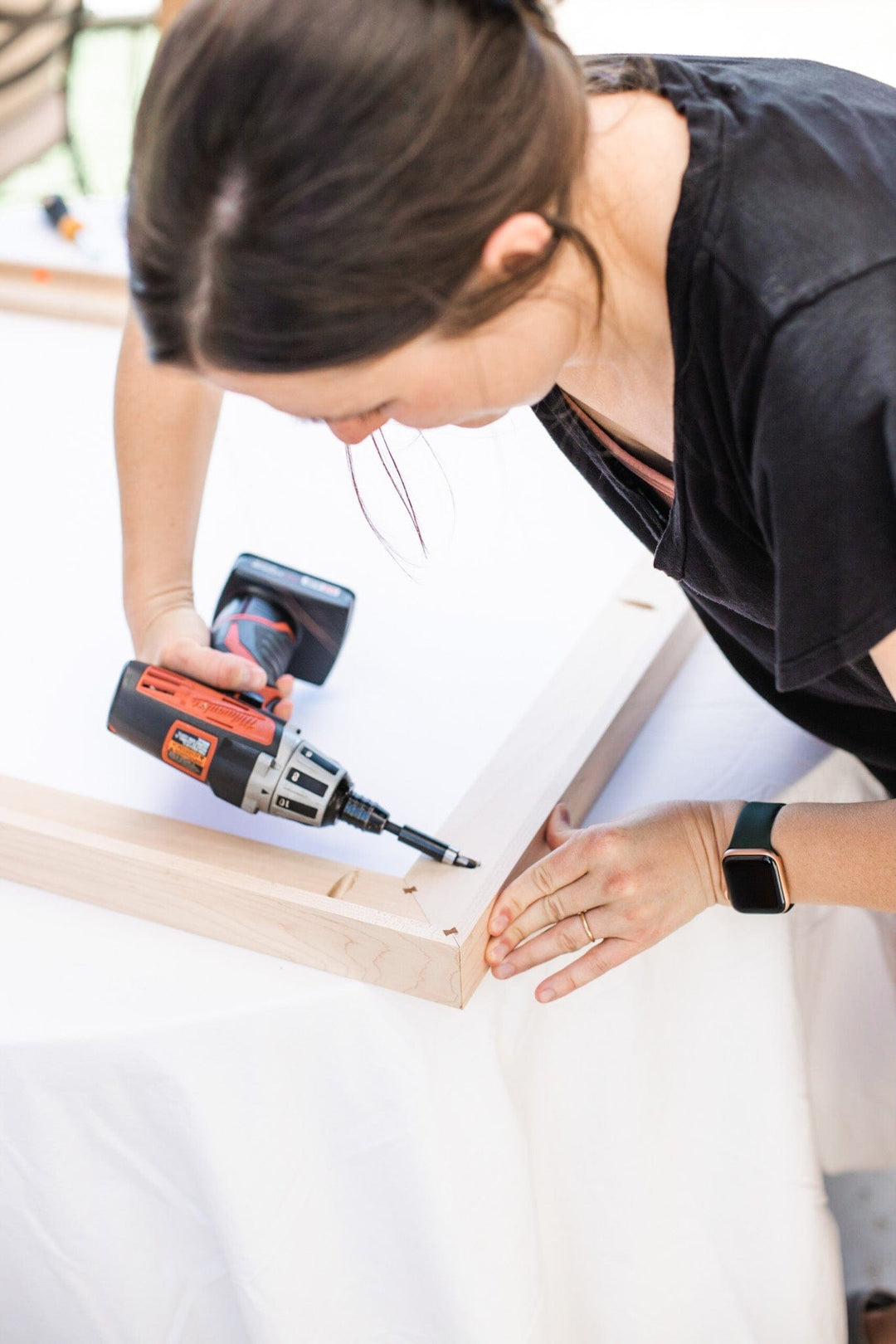 Woman using a drill on wood frame.