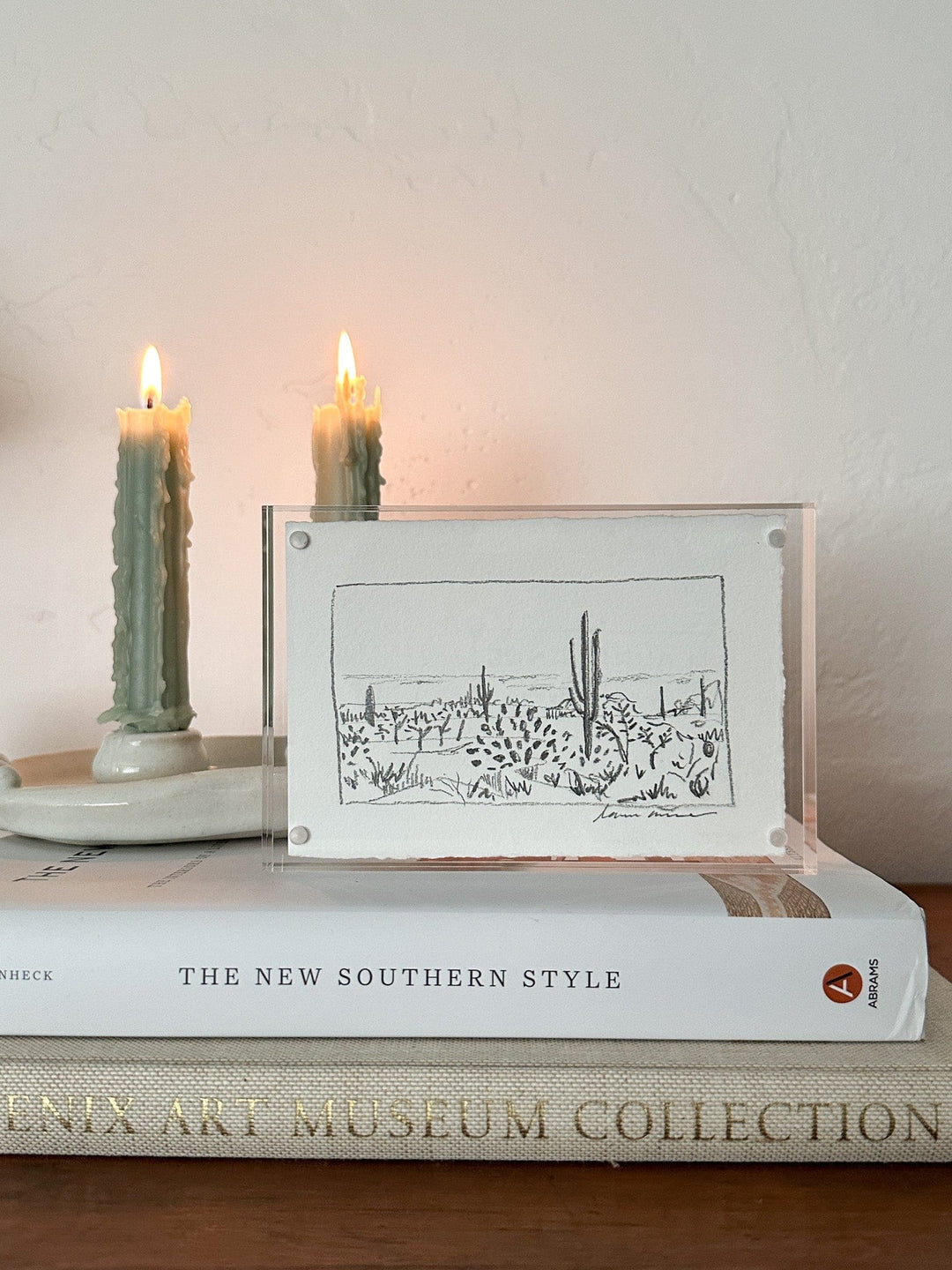 Candles and desert landscape artwork on a book.