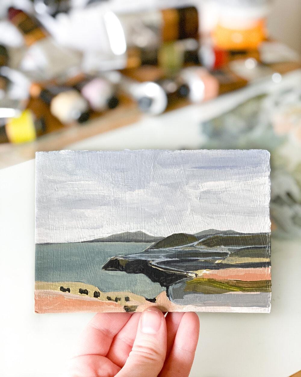 Hand holding a small landscape painting.