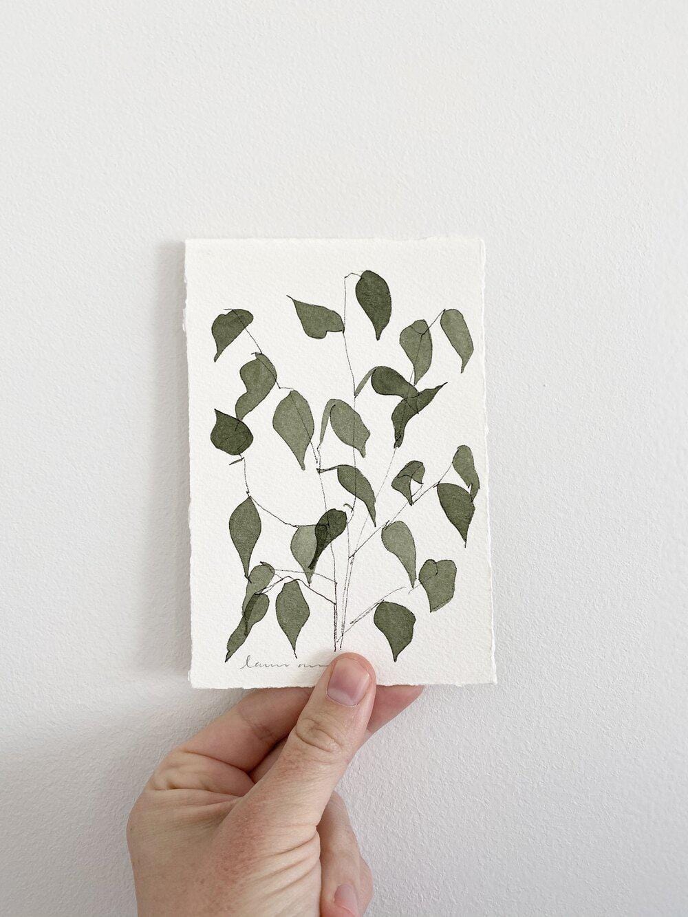 Hand holding watercolor painting of leaves.
