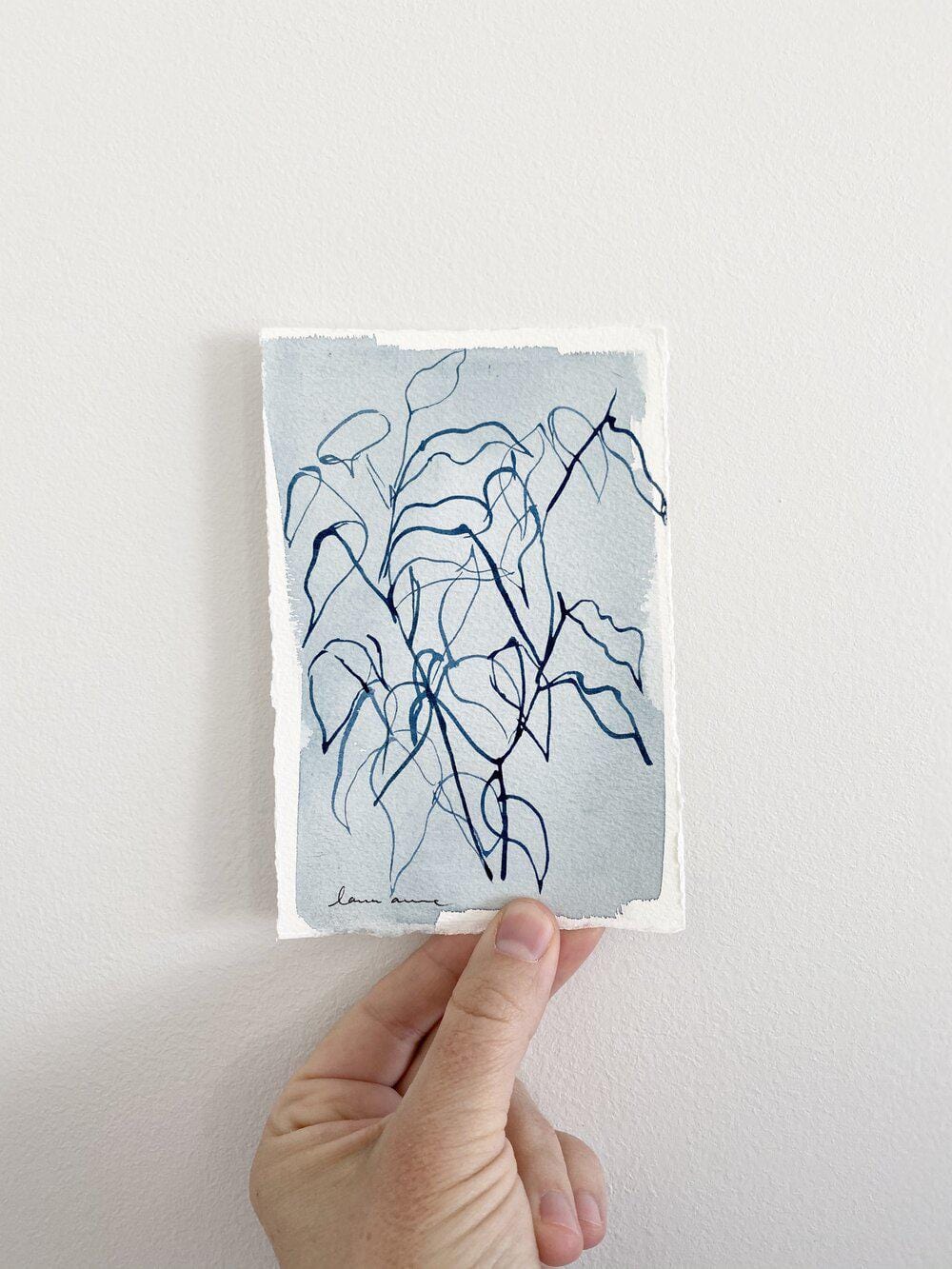 Hand holding a blue ink drawing of a plant.