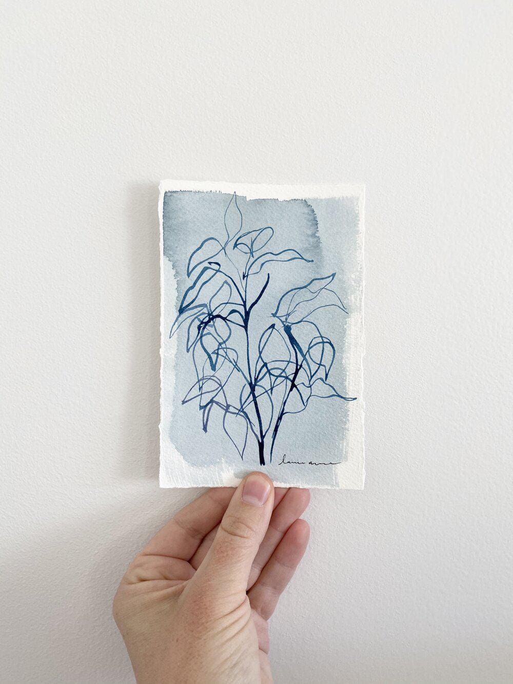 Hand holding a watercolor painting of a plant.