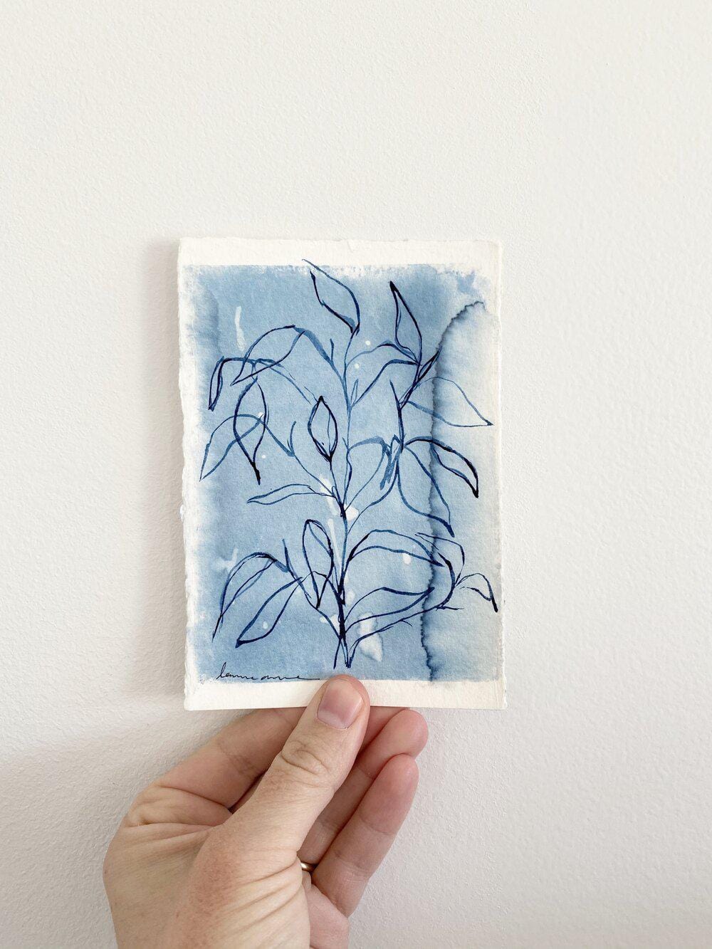 Hand holding a watercolor painting of a plant.