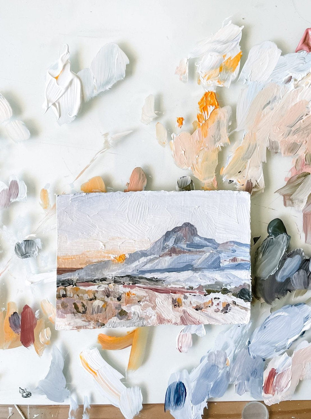Miniature mountain landscape painting surrounded by paint splotches.