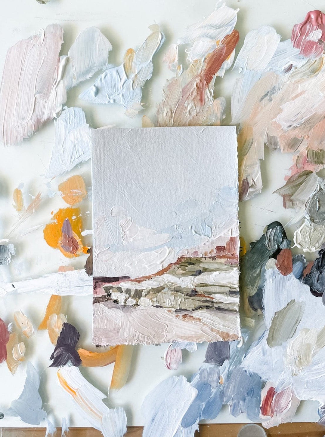 Small landscape painting on a palette of mixed paint colors.