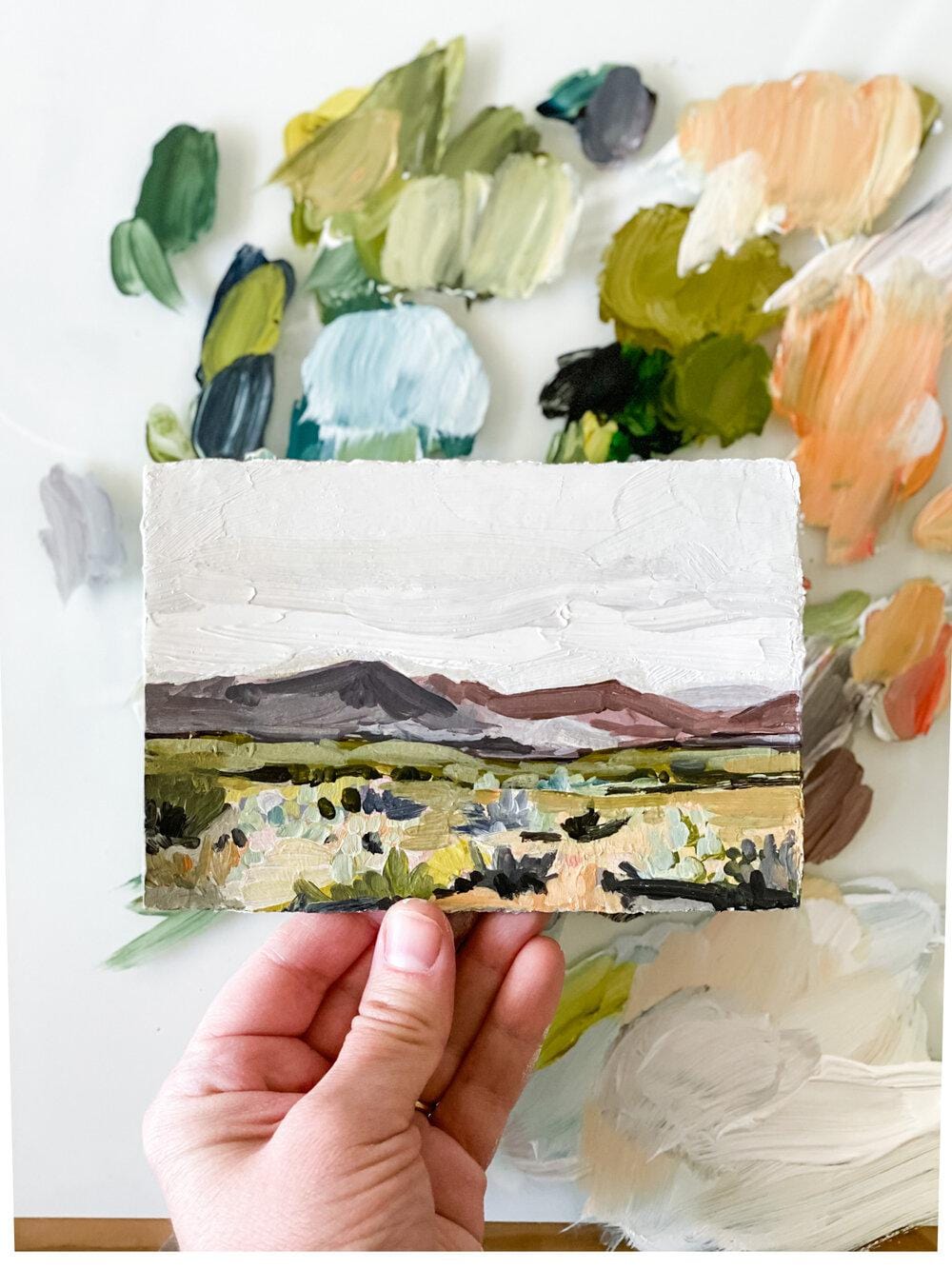 Hand holding landscape painting with paint palette.