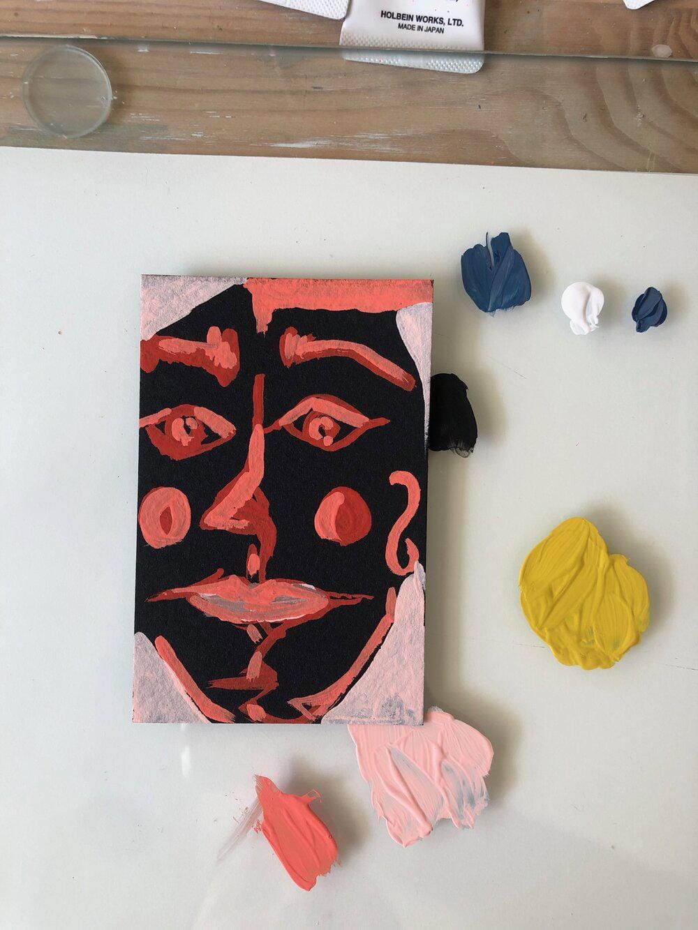 Painting of a face with paint splotches on a white surface.
