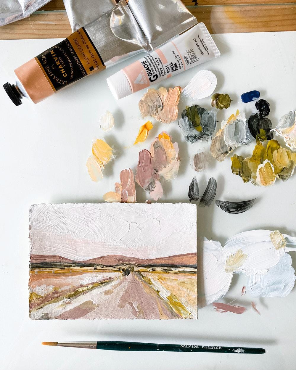 Paint tubes, palette of paint, landscape painting, and brush.