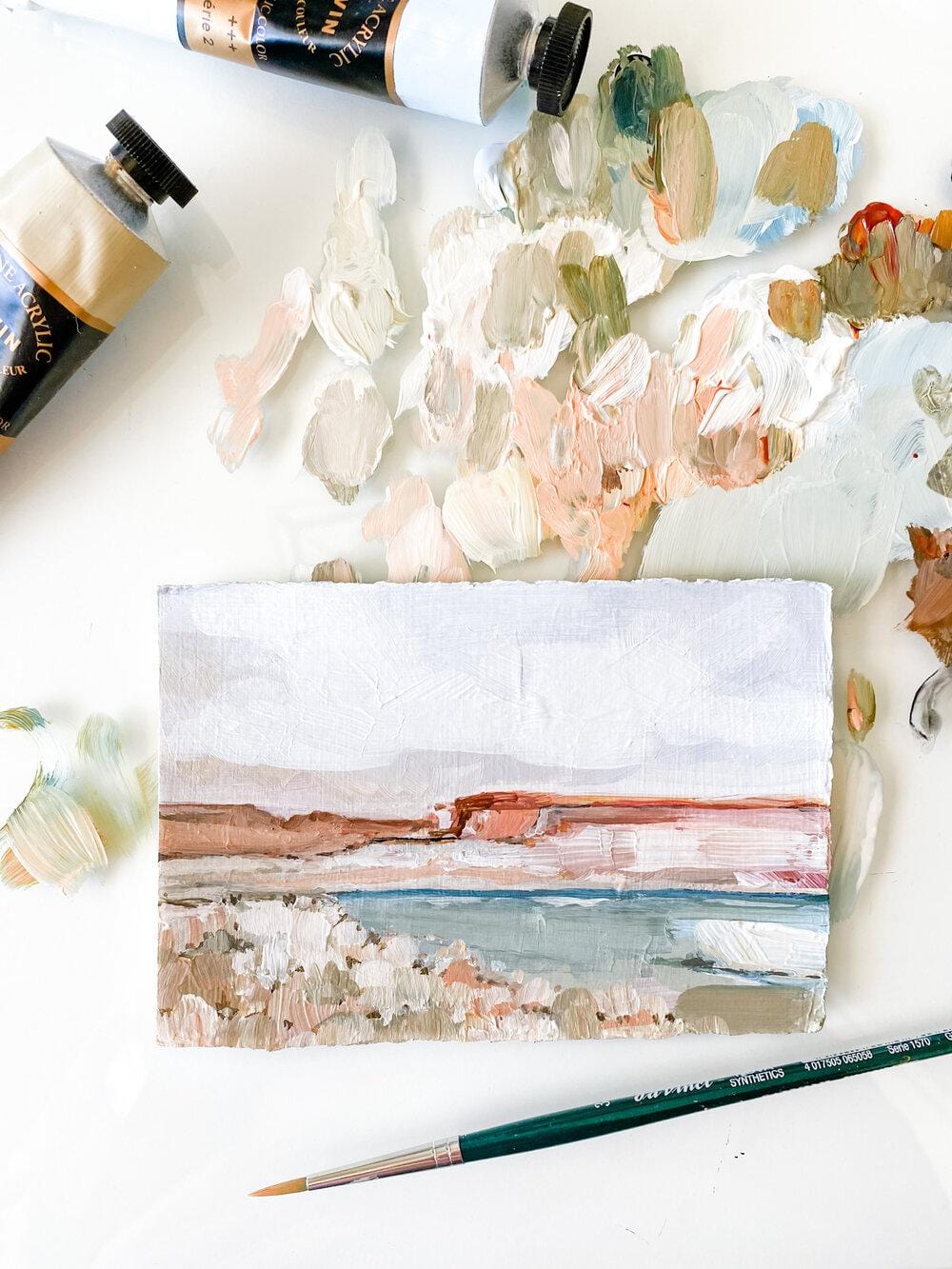 Coastal landscape painting with paint tubes and palette.