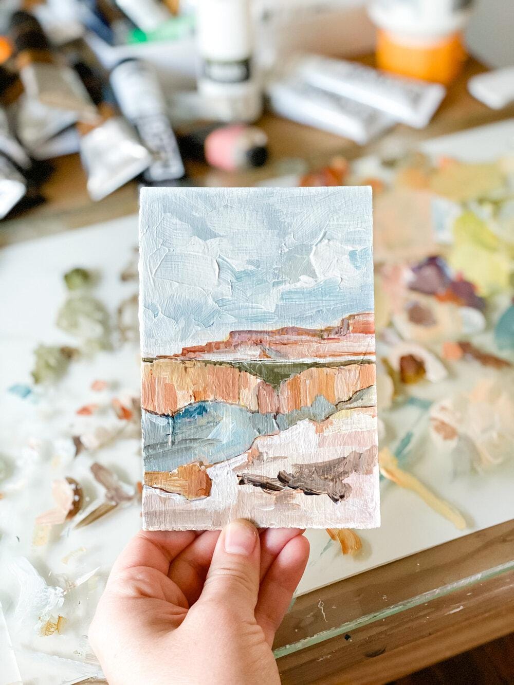 Hand holding a small landscape painting.