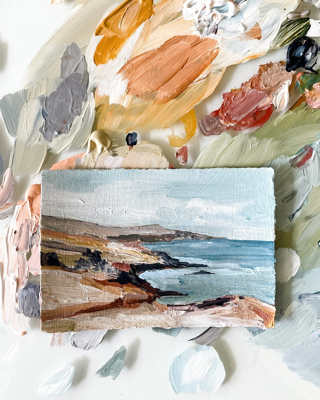 Coastal landscape painting surrounded by paint palette.