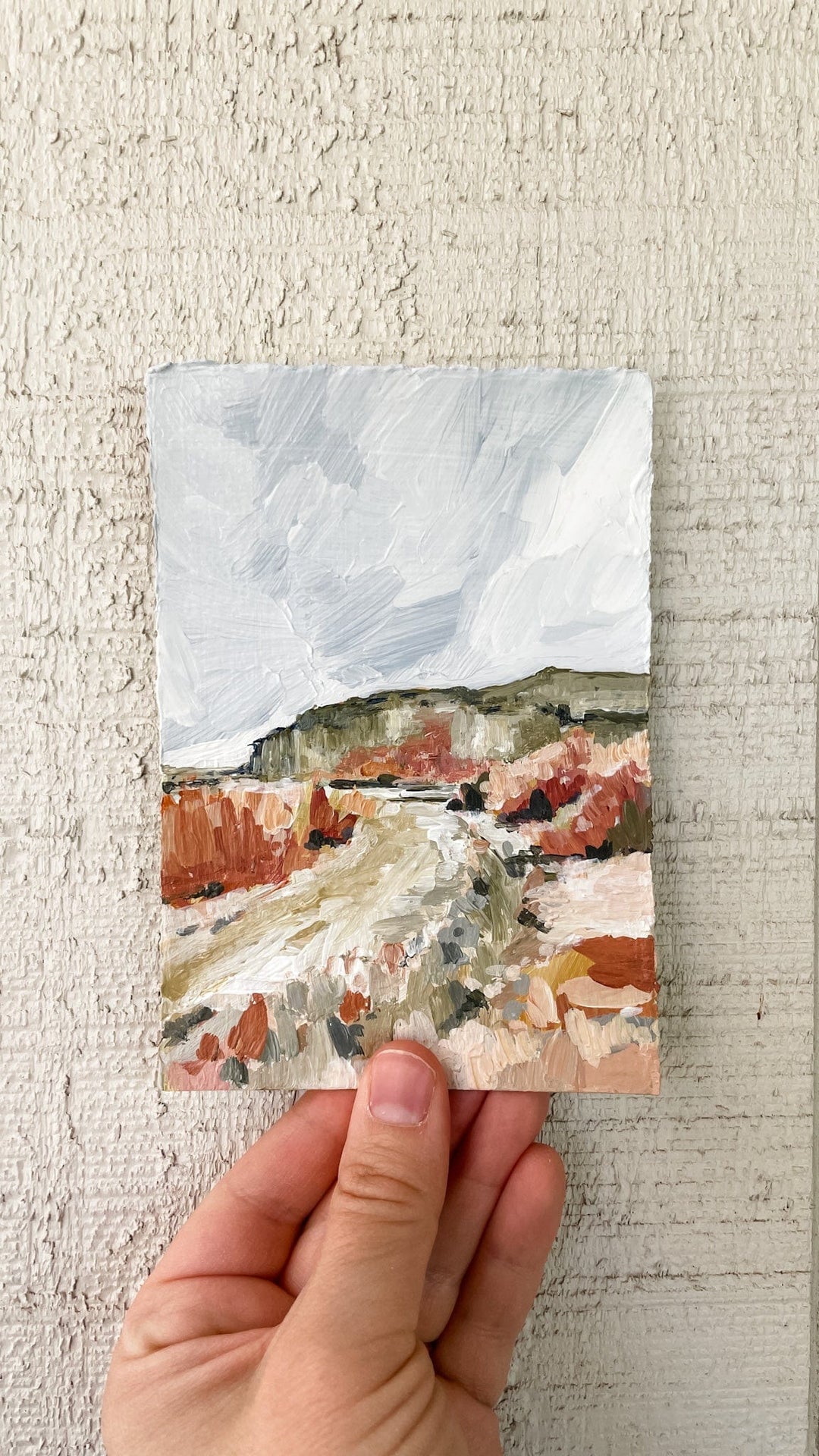 Hand holding a landscape painting of a desert scene.